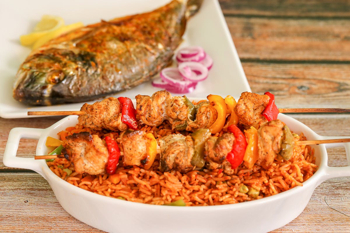 A plate of jollof rice with grilled skewers and fish